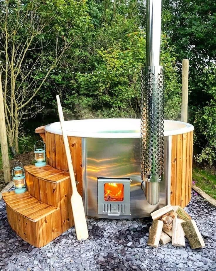 Wood-fired hot tub with its integrated stove lit and split logs stacked alongside