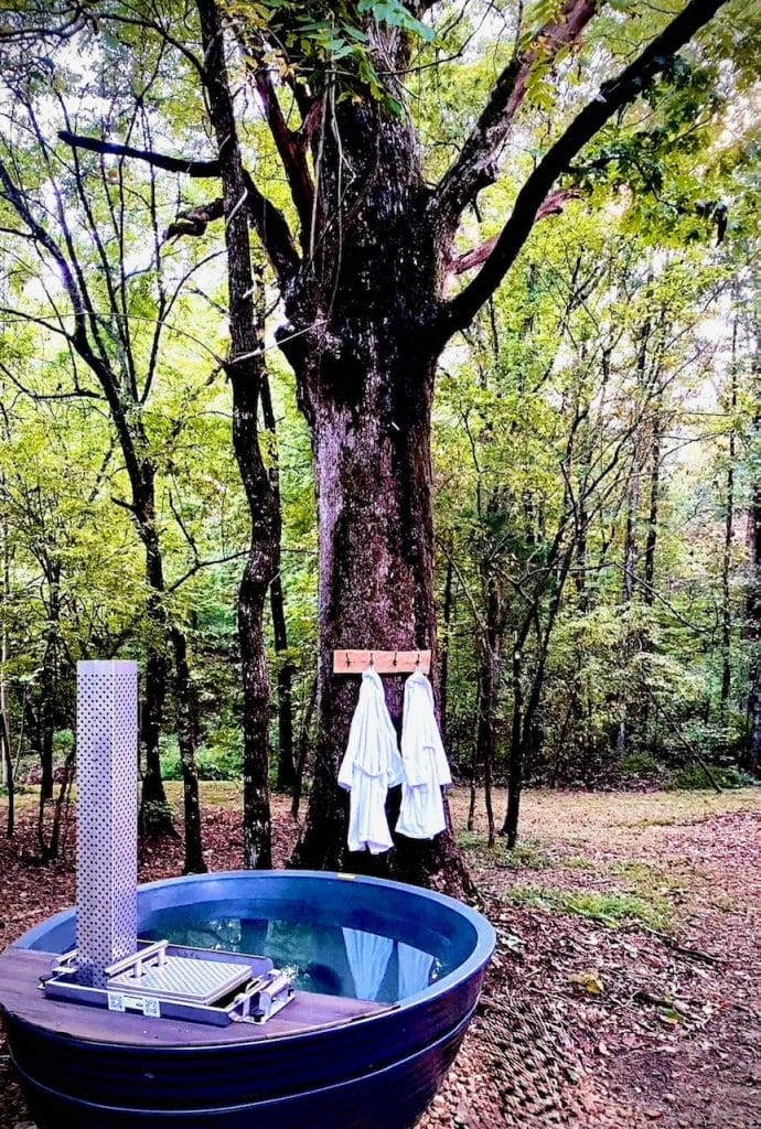 Wood-fired tub with external heater set among trees, towels hanging on the trunk