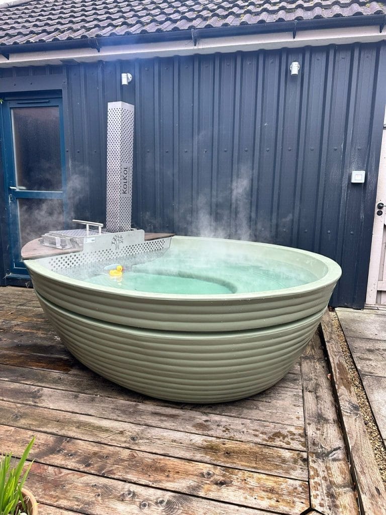 How long a wood-fired hot tub takes to heat up, steaming green tub on a deck
