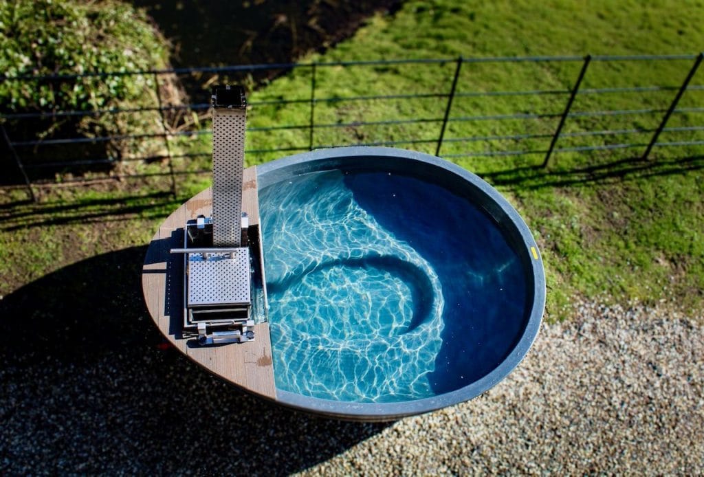 Overhead view of a filled wood-fired tub with external heater in a rural garden